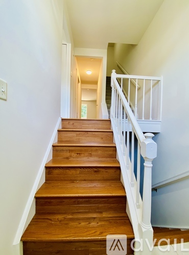 A wooden staircase with white railings leads to a bright hallway.
