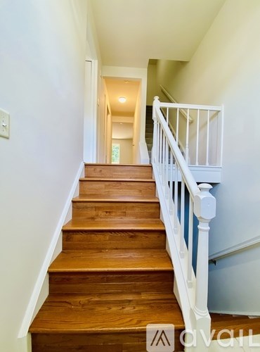 A wooden staircase with white railings leads to a bright hallway.