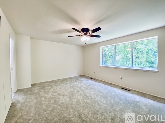 A room with a ceiling fan and a window overlooking trees.
