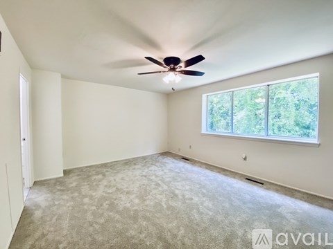 A room with a ceiling fan and a window overlooking trees.