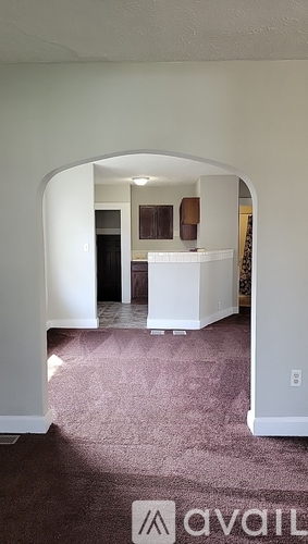 A room with a carpeted floor and a white archway leading to another room.