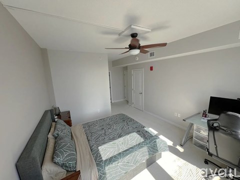 A bedroom with a bed, desk, and ceiling fan.