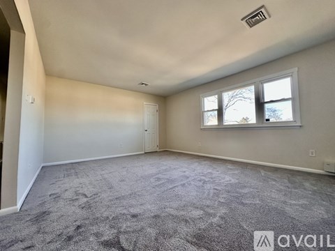 A spacious room with a carpeted floor, a window with a view of trees, and a ceiling fan.