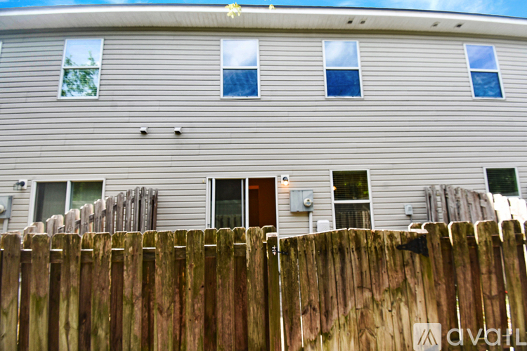 A wooden fence in front of a grey building with four windows.