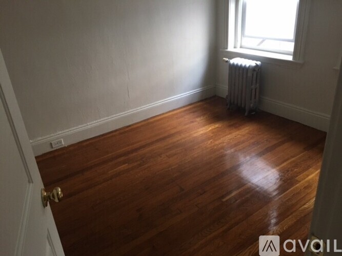 A room with wooden floors and a window with a radiator beside it.