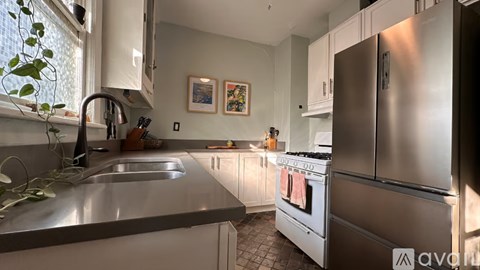 A kitchen with a stainless steel refrigerator and a sink with a plant on the counter.