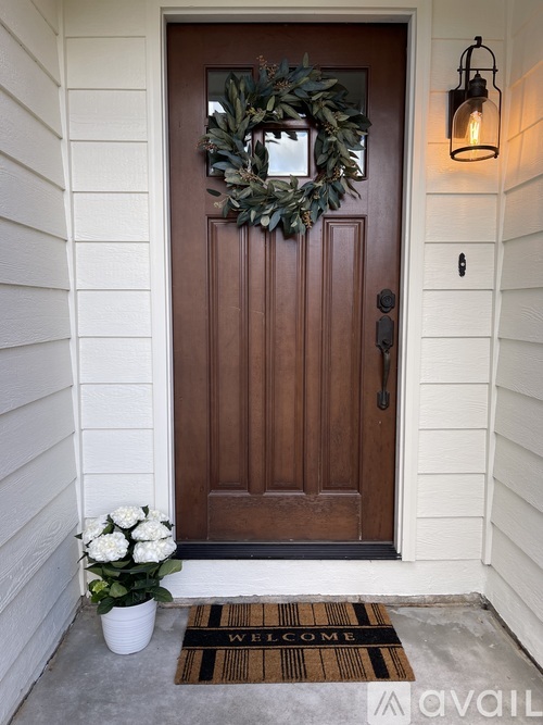 A brown door with a wreath on it and a welcome mat in front.