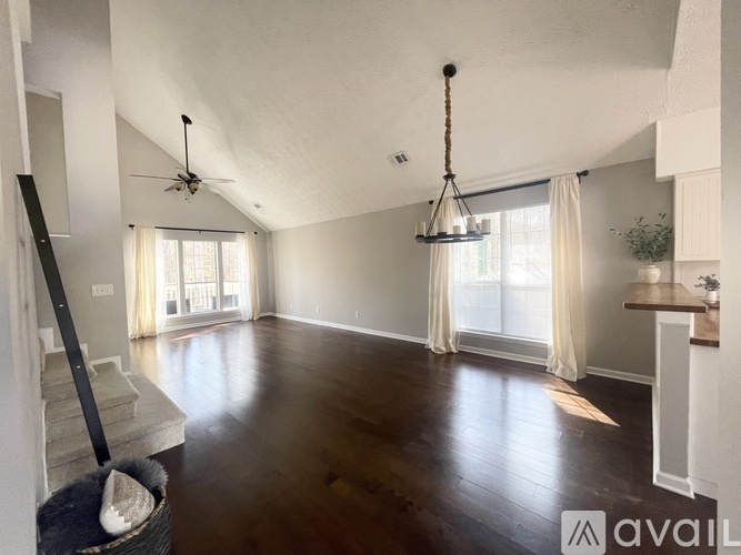 A spacious living room with a staircase on the left and a chandelier hanging from the ceiling.