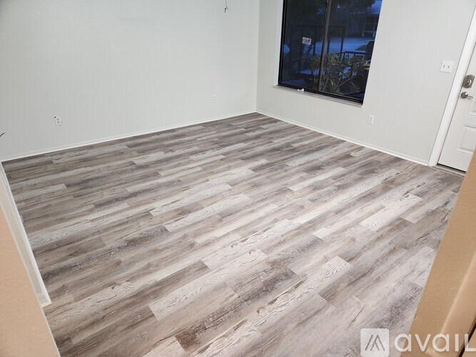 A room with a wooden floor and a window showing trees outside.