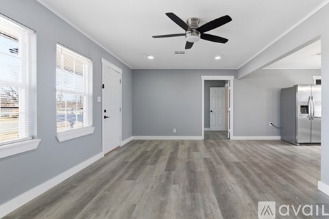 A spacious room with a ceiling fan and lighting, and a kitchenette in the corner.