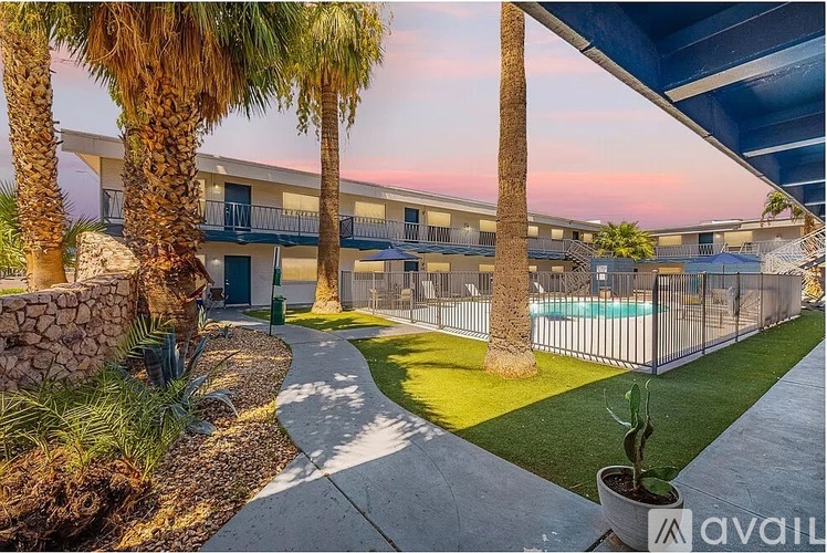 A sunset view of a pool surrounded by palm trees and apartment buildings.