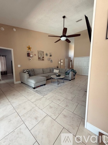 A living room with a beige couch, a white rug, and a ceiling fan.