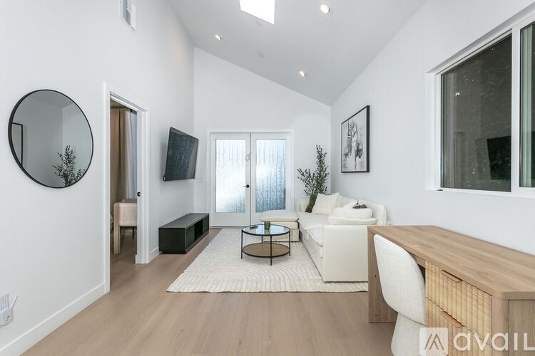 A modern living room with a white sofa, a wooden table, and a large mirror on the wall.