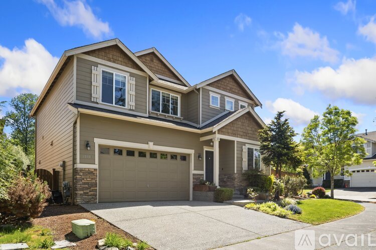 A two-story house with a garage is surrounded by a well-kept lawn and trees.