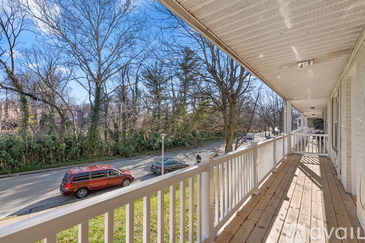 A red car is driving down the street next to a white fence.