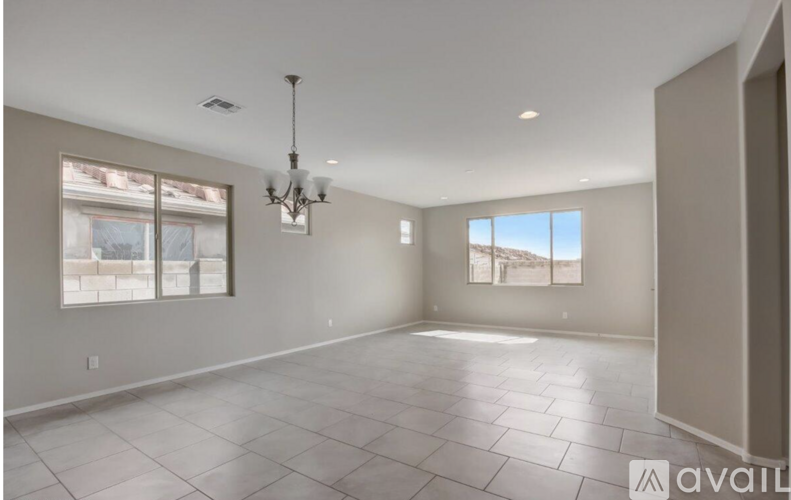 A spacious room with a chandelier, tiled floor, and large windows.