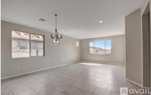 A spacious room with a chandelier, tiled floor, and large windows.