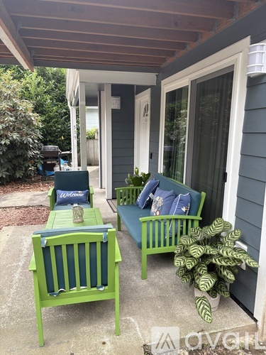 A green bench with a pillow and a potted plant sits on a porch.