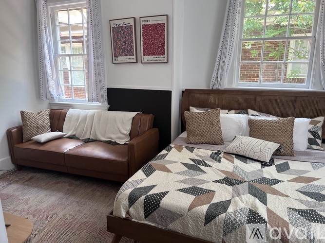 A bedroom with a brown leather couch and a bed with a quilt on it.