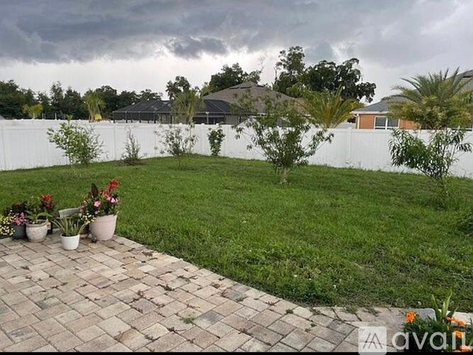 A backyard with a brick walkway and a white fence.