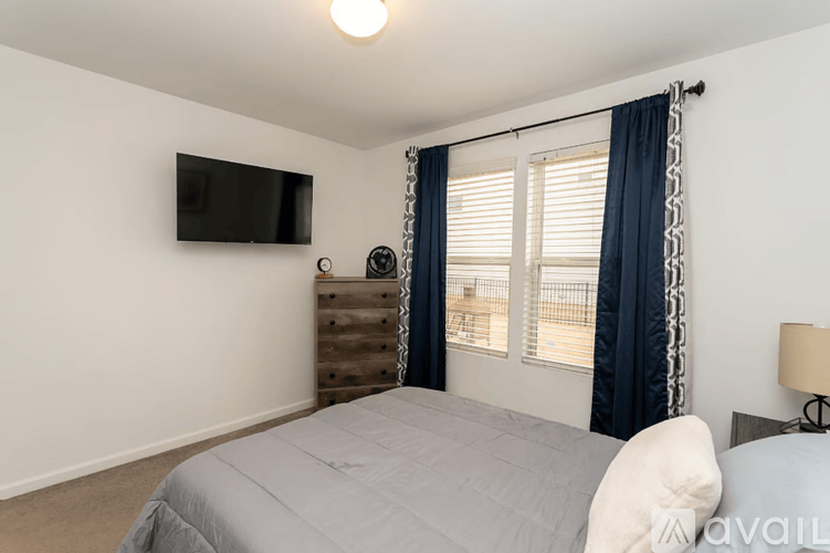 A bedroom with a bed, a television, and a window with blue curtains.