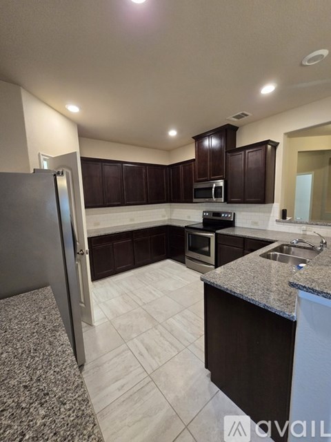 A kitchen with granite countertops and dark brown cabinets.