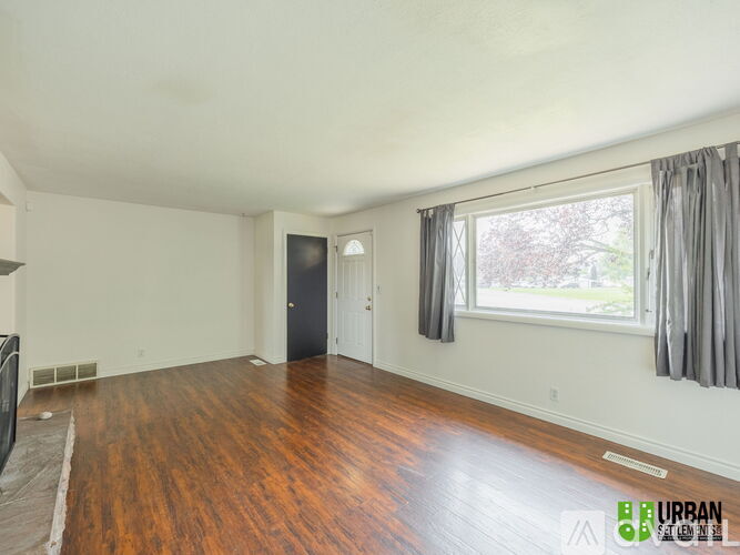 A spacious room with wooden floors and a large window with curtains.