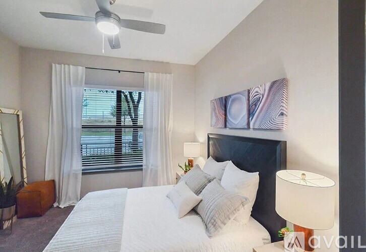 A bedroom with a large bed, a ceiling fan, and a window with white curtains.