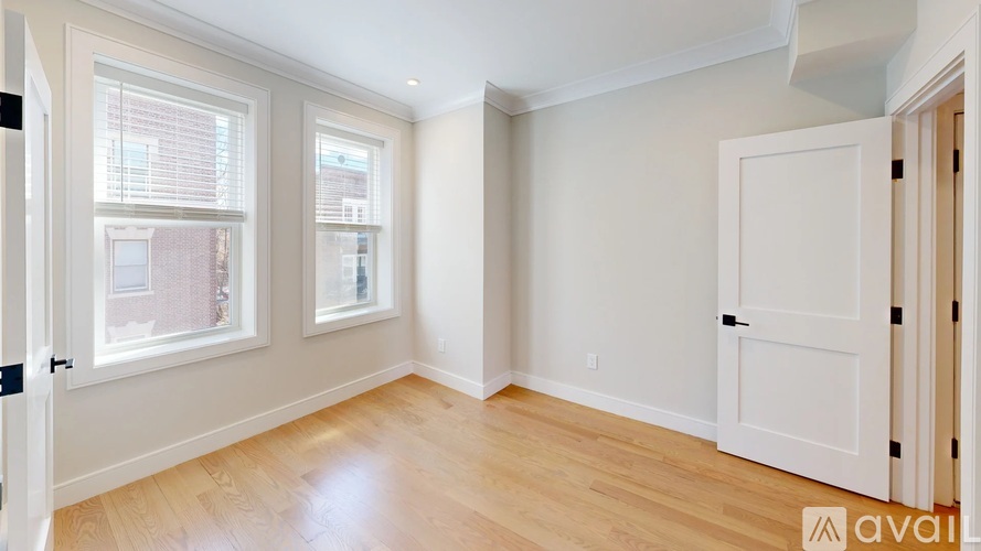 A room with wooden floors and white walls, with a window showing a view of a building outside.