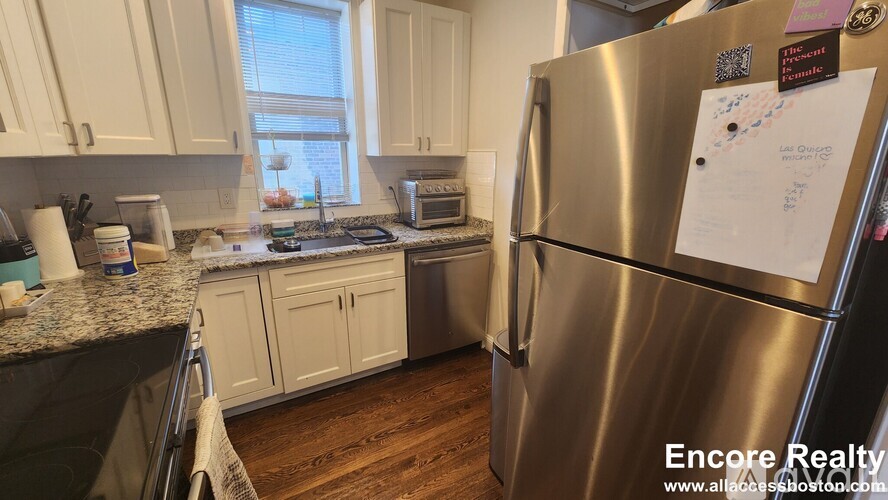 A kitchen with a stainless steel refrigerator and wooden floors.