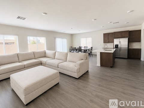 A spacious living room with a large white sofa and a kitchen area in the background.