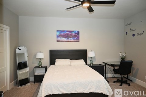A bedroom with a large bed, a desk with a chair, and a ceiling fan.