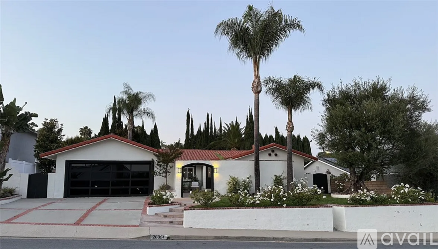 A house with a red tile roof and a garage door is surrounded by palm trees.