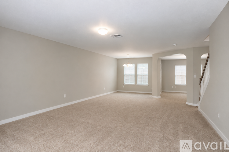 A spacious room with beige carpeting and a staircase on the right side.