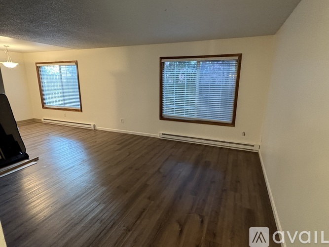 A room with wooden floors and two windows with blinds.
