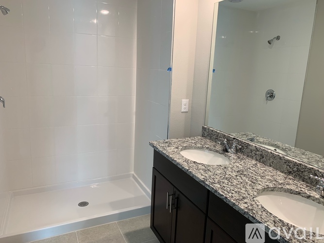 A bathroom with a white tiled shower and a granite countertop with two sinks.