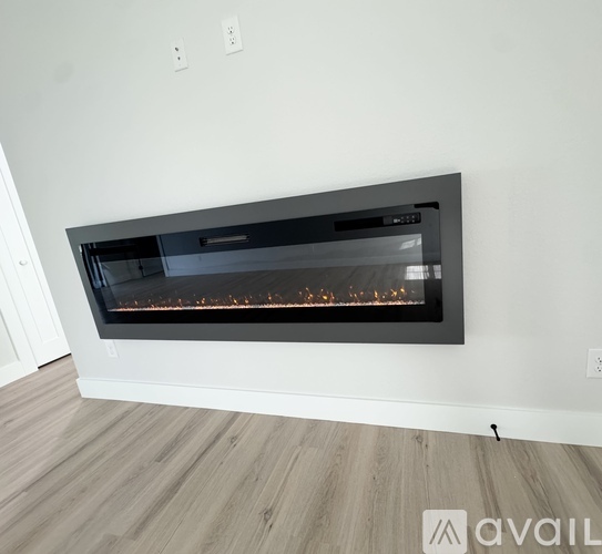 A modern fireplace with a black frame and a glass door is installed in a room with wooden flooring and white walls.
