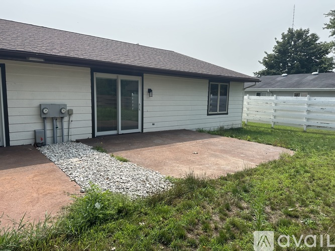 A house with a grey siding and a brown roof with a white fence in the background.