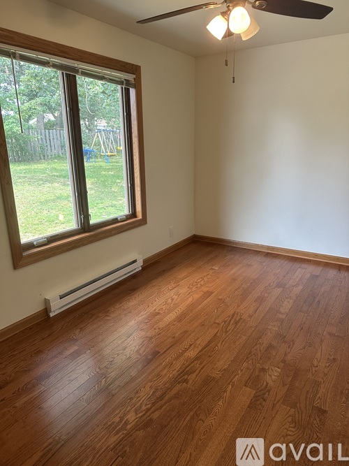 A room with wooden flooring and a window overlooking a backyard.