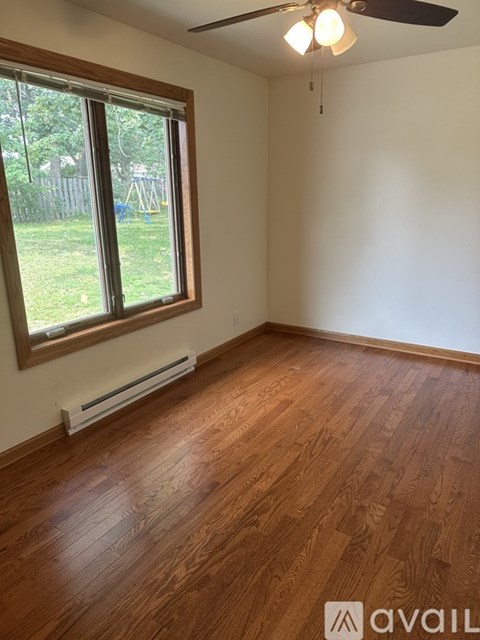 A room with wooden flooring and a window overlooking a backyard.