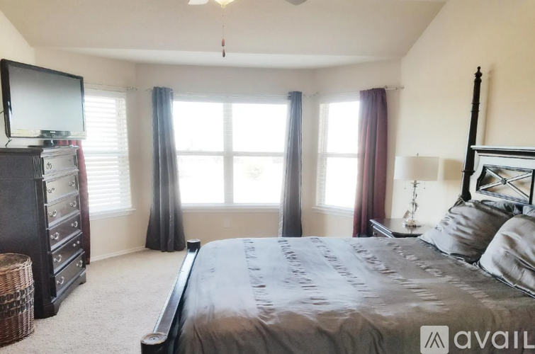 A bedroom with a large bed, a television, and a window with curtains.