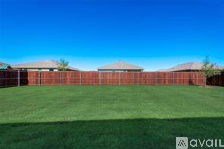 A large grassy field with a fence and buildings in the distance.