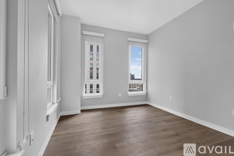 A spacious room with wooden flooring and a window with a view of the city.