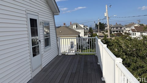 A white house with a deck and a view of the neighborhood.