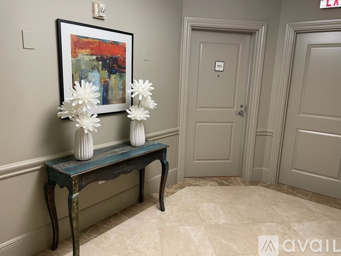 A painting hangs on the wall above a bench with a vase of flowers on it.