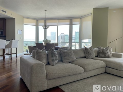 A large beige couch with multiple pillows sits in a spacious living room with a view of the city.