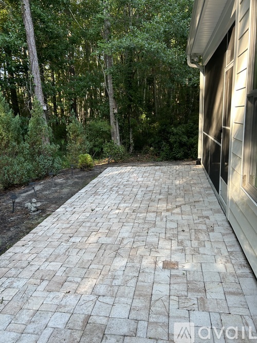 A brick pathway leads from a house into a wooded area.