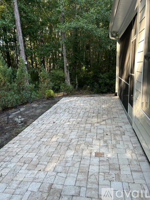 A brick pathway leads from a house into a wooded area.
