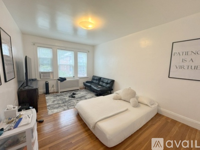 A bedroom with a bed, couch, and a wall hanging that says "Patience is a virtue".
