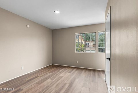 A room with wooden flooring and a window showing a view of a building outside.